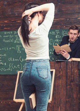 Arka görünümü güzel popo bir at kuyruğu bacaklarının arasında bir kitap tutarken yapma kızla. Arka planda bulanık açıklamalar veren öğretmen