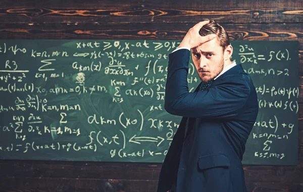 Nachdenklicher junger Mann im eleganten Anzug, der über eine grüne Tafel voller Schriften steht. Besorgter intelligenter Professor hält die Hand auf dem Kopf — Stockfoto