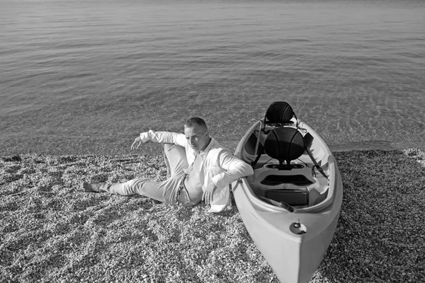 Sommerurlaub und Schiffsreise. Macho-Mann genießt Sommertag auf Sand. Sexy Mann am Meer Wasser in der Nähe von Boot. Mann entspannen am Strand Sand. Bootsfahrt des Athleten. — Stockfoto