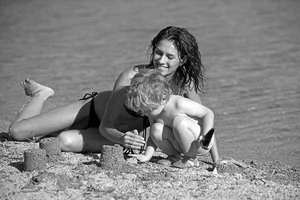 Een jongen make zand Kasteeltje bij actieve moeder, langs de waterkant op het strand. Het kind voelt zo trots dat hij met zijn moeder houden kan — Stockfoto