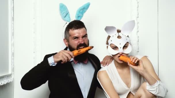 为复活节做准备的幸福夫妇。复活节那天的兔子。像野兔一样咬胡萝卜。复活节快乐。孤立。有趣的兔子和胡萝卜的概念。可爱的夫妇穿着小兔子在复活节. — 图库视频影像