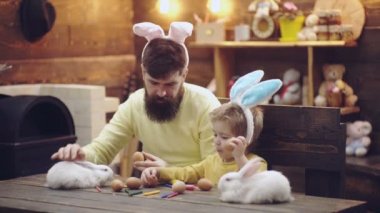 Baba ve oğul boyalı Paskalya yumurtaları ve Paskalya tavşanı ile oynamak. Mutlu bir aile Paskalya için hazırlanıyor. Sevimli küçük çocuk çocuk bunny kulaklar giyiyor. Ahşap arka plan üzerinde Paskalya yumurtaları.