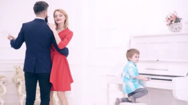 Çocuk çocuk piyano çalıyor ve ailesi dans. Yatak odasında Piano oyunu. Müzik aile evde eğleniyor. Aile Evde dinleniyor. Mutlu aile kavramı. Aile çift dans. Çocuk Piyano çalıyor.