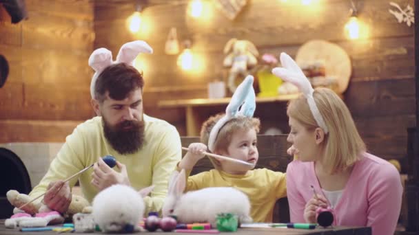 Mor, far och son målar påskägg. Lycklig familj förbereder för påsk. Söt liten barn pojke bär bunny öron. Förbereder för påskfirande. Påskägg på trä bakgrund. — Stockvideo