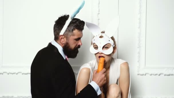 Couple with rabbit ears isolated on white background. Easter rabbits. Bunny couple. Happy couple preparing for Easter. Lovely man in rabbit costume is feeding his girlfriend bunny with carrot.