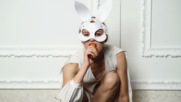 Woman in a leather mask of rabbit eats carrots isolated on white background. Easter, makeup, pinup party, girl in rabbit ears. Easter rabbits. Nibbles a carrot like a hare. Happy Easter. — Stock Video