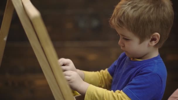 Primer plano de un chico que escribe con tiza en una tabla. Precioso dibujo de niño pequeño en pizarra sobre fondo de madera. Pequeño artista pinta sobre un fondo de madera. Concepto de creatividad y bellas artes . — Vídeos de Stock