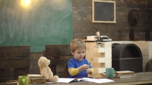 Koncentrerad Kid skriver i copybook. För skola pojke sitter vid Skriv bordet. Läro brev på dagis. Pojke ritning på bakgrund av en skol styrelse. Tillbaka till skolan. Läraren kan göra varaktiga effekter. — Stockvideo