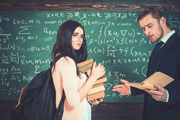 교수를 읽는 동안 책의 더미를 들고 안경을 쓰고 분홍색 카디 건 젊은 갈색 머리. 녹색 보드 앞에 서 있는 교사 및 대학 여자 — 스톡 사진