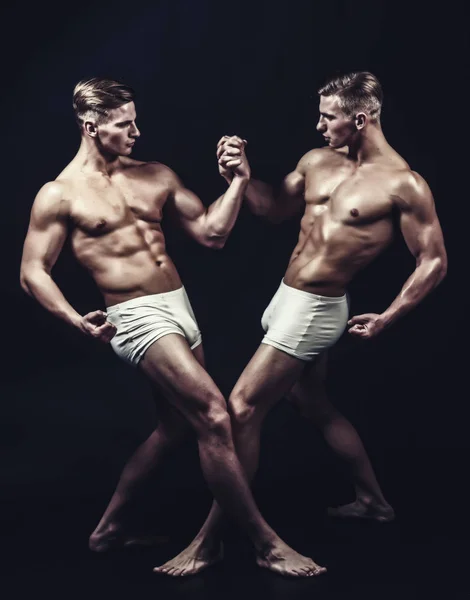 Twins mannen met gespierd lichaam in evenwicht vormen. tweeling gespierde mannen in bodybuilder vormen geïsoleerd op zwarte achtergrond. — Stockfoto