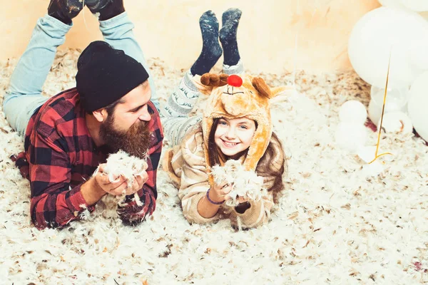 Winter party and eve. Father and daughter lie in feathers, christmas. Man hipster and child smile at xmas. Family holiday party. Fathers day celebration. Happy family celebrate christmas and new year