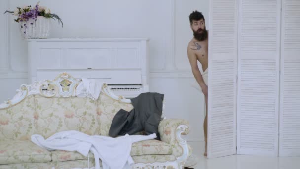 Man, lover in white interior caught naked. Exposing lovers concept. Hipster naked on shocked face unexpectedly detected in bedroom. Man with beard and mustache hiding behind folding screen. — Stock Video