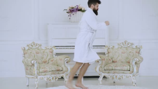 Concept d'exercice matinal. Un homme barbu en robe de chambre blanche court dans une pièce sur un fond de piano blanc. Concept de mode de vie sain. L'homme drôle court. macho énergique et réussi . — Video