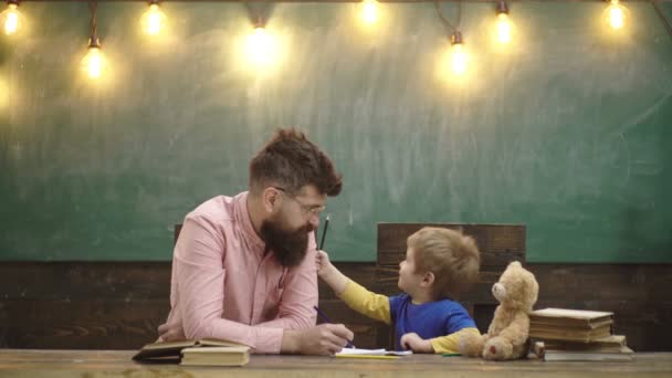 Profesor y niño pequeño escribiendo cartas en copybook. Lindo chico dibujando un cuadro con lápices de colores. Clase de arte en el jardín de infantes. Concepto de arte. Profesor mostrando a niño cómo delinear mano sobre papel . — Vídeos de Stock