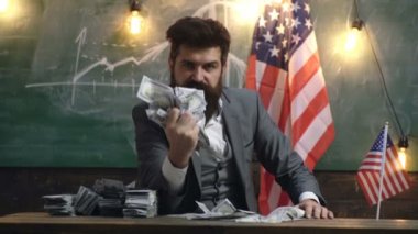 Elbiseli adam ABD bayrağı arka planı kötü yüz ifadesi ile elinde bir tomar para sıkar. Vatanseverlik ve özgürlük. Finansal Yönetim, küresel finansal akışları ve güç.