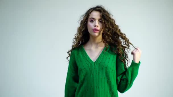 Fashion woman in green sweater. Cheerful beautiful girl with curly hair, braces on her teeth, wraps hair on a finger, smiling broadly with her mouth open. Concept fun, happiness, laughter. — Stock Video