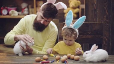 Baba ve oğul Paskalya yumurtaları boya vardır. Sevimli küçük çocuk çocuk bunny kulaklar giyiyor. Paskalya yumurtaları ahşap arka plan üzerinde. adam ve bir çocuk arıları ve tavşan kulakları Paskalya için hazırlanıyorlar.