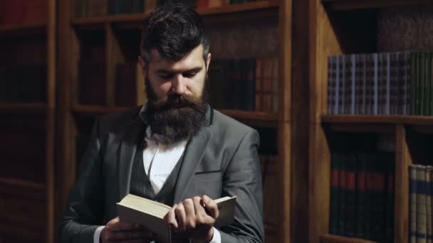 Homme avec livre de lecture de barbe sur fond de bibliothèque. Un homme lisant un livre à la bibliothèque. Portrait d'un homme du collège lisant un livre à la bibliothèque. Étudiant hipster étudiant à la bibliothèque de l'université . — Video