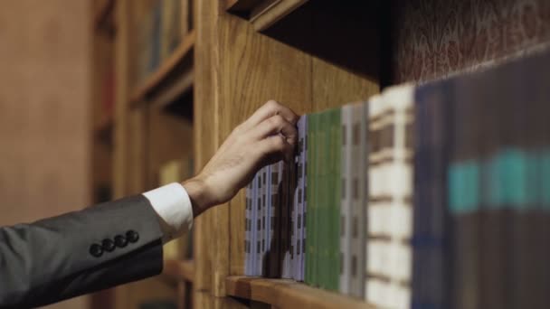 Mano derecha masculina que elige y escoge el libro en la biblioteca pública. Sacando el libro de texto seleccionado. Investigación educativa y autoaprendizaje en conceptos de vida universitaria. Concepto de educación y biblioteca . — Vídeo de stock