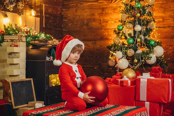 Un niño confuso lleva ropa de Santa Claus, decorando el árbol de Navidad. Concepto de Navidad. Chico de Navidad. Navidad niños sueños . — Foto de Stock