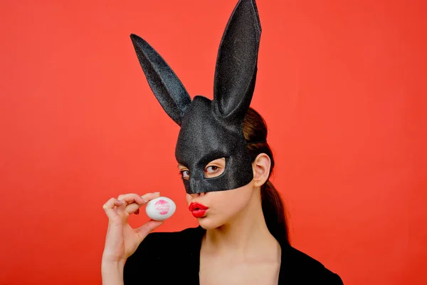 Pasen vrouw. Vrouw konijn, easter bunny meisje. Rode lip afdruk op easter egg op rode achtergrond. Vrouwelijke mond kus. Afdrukken van rode lippen op witte ei. — Stockfoto