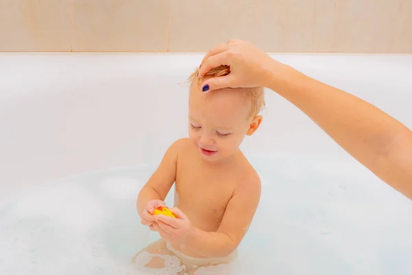 1-jarige baby baadt in een douche. Kleine nieuwsgierig mooie baby zit in witte badkamer met natte schuim haren op zoek weg. Gezonde jonge geitjes. — Stockfoto