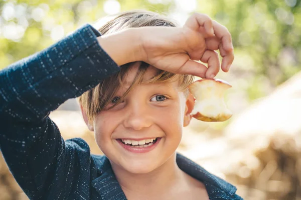 Bambino in vacanza autunnale in agriturismo. Un ragazzo sorridente tiene una mela morsa con una mano. Ciao estate - ciao autunno. Vendita per tutta la collezione autunnale, sconti incredibili e scelta meravigliosa . — Foto Stock