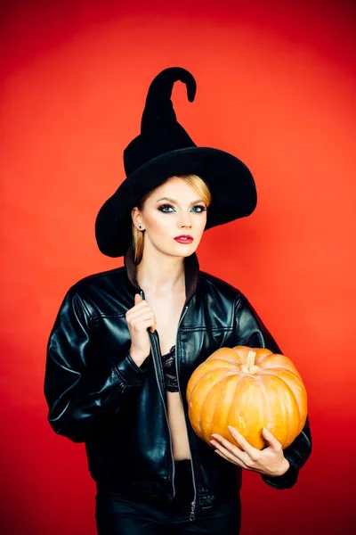 Jonge vrouwen in zwarte heks halloween kostuums op feest over rode achtergrond. Heks poseren met pompoen. — Stockfoto