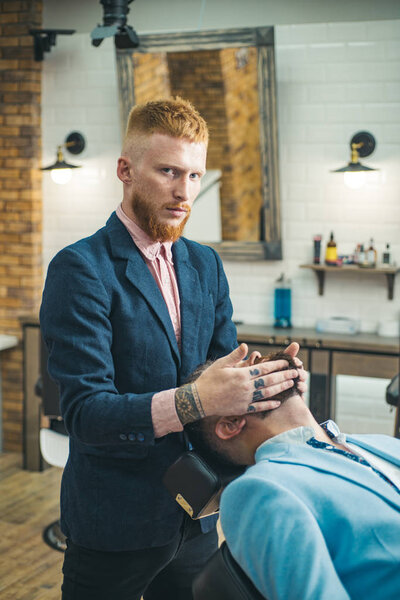 Barber Shop Studios. Barber shaving a bearded man in a barbershop. Beard man visiting hairstylist in barber shop. Barbershop.
