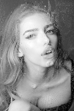 Pencere cam kız yüzü ile yağmur damlaları. Moda ve güzellik. Kız makyaj ile daha önce su ile pencere bırakır. Su ile plastik levha arkasındaki seksi kadın bırakır. Duş ve hijyen kaplıca tedavisi