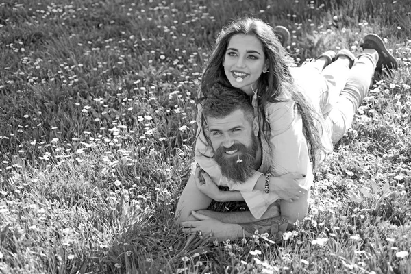 Man and woman laying on grass spring day. Spring leisure concept. Couple on happy faces laying at meadow with daisy flowers in mouth, nature on background. Couple in love spend time outdoors and hugs.