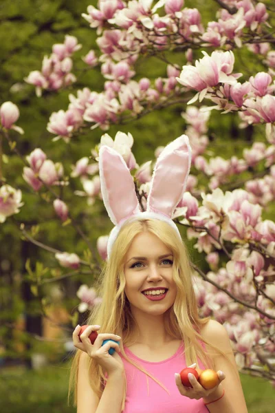 Mujer con huevos de Pascua en orejas de conejo en flor de magnolia — Foto de Stock