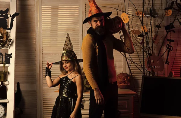 Wizard and little witch in hats hold pumpkin