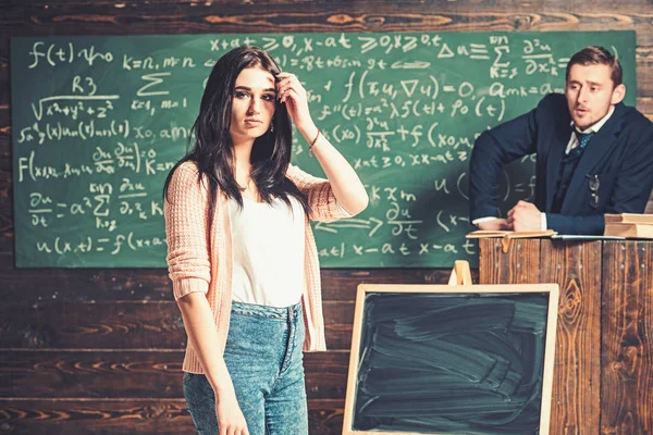 Jeune étudiante en cardigan rose et jean bleu debout devant la planche verte. Brunette adolescente dans la salle de classe écouter des explications — Photo