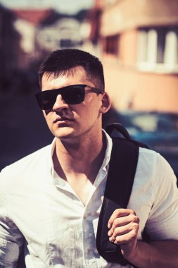 Yakışıklı şık beyaz adam omuzlarında sırt çantası ile sokak arka plan karşı poz trendy güneş gözlüğü takıyor. Gezgin adam şehirde. Yaşam tarzı moda kentsel kavramı