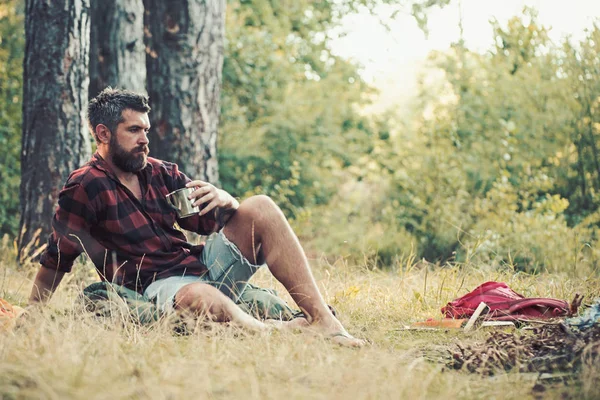 Hipster trinken Tee oder Kaffee am Lagerfeuer. bärtige Männer entspannen mit einem Becher am Lagerfeuer. Typen zelten gerne im Wald. Sommerferienkonzept. Zelten, Wandern und Reisen — Stockfoto