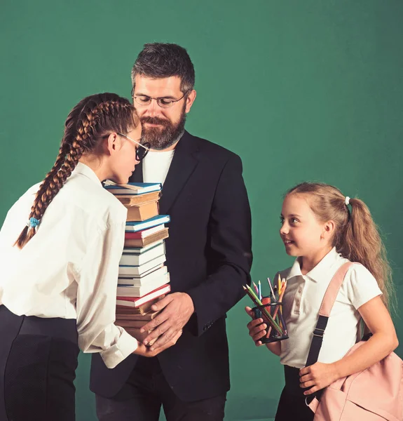 Teacher man and girls hold book pile at school. teacher gives pile of book to schoolgirls on green background