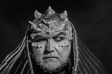 Beyaz sakallı komuta sizde canavar gibi giyinmiş. Adam dikenler veya siğiller ile yüz pırıltılar ile kaplı. Fantezi kavramı. Siyah zemin üzerine altın kukuleta ile iblis. Uzaylı, iblis, büyücü makyaj.