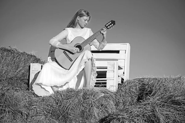 Músico de moda en vestido blanco en la naturaleza soleada. Mujer guitarrista realizar concierto de música. Chica albina sostener la guitarra acústica, instrumento de cuerda. Sensual mujer tocar la guitarra en banco de madera — Foto de Stock