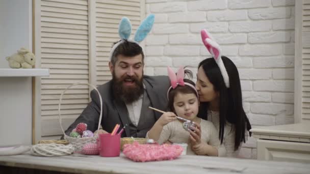 Mor, far och dotter målar påskägg. Lycklig familj förbereder sig för påsk. Söt liten barn flicka bär bunny öron. Glad påsk stämning. Glad familj på tröskeln till påsk. — Stockvideo