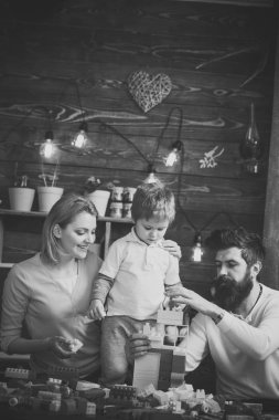 Aile oyun ile plastik blok birlikte. Sevimli oğlu tarafından omuz tutan güzel gülümseyen anne. Sarışın çocuk babası kuleden inşaat tuğla bina izlerken