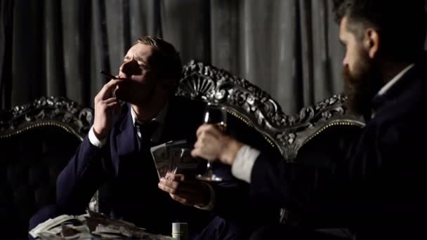 豪華な男性がソファーに座って、メンズクラブで葉巻を吸って、地球規模の問題を解決します。成功した2人のビジネスマンのビジネスとグローバルな陰謀の共謀。ビジネス、お金のコンセプト. — ストック動画
