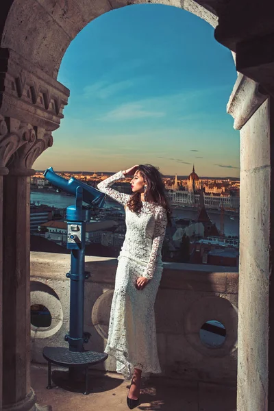 Modèle de mode Voyage en vacances. Femme avec télescope au point de vue sur le paysage urbain. Femme sensuelle aux cheveux longs en robe de mariée blanche, mode. Fille avec look glamour, maquillage, beauté . — Photo