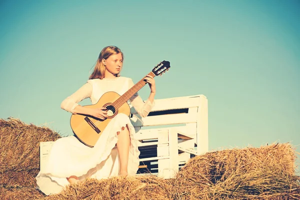 Sensual woman play guitar on wooden bench. Albino girl hold acoustic guitar, string instrument. Fashion musician in white dress on sunny nature. Woman guitarist perform music concert