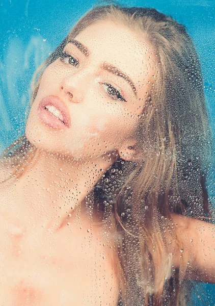 Fashion and beauty. Window with water drops before girl with makeup. Rain drops on window glass with face of girl. Shower and hygiene spa treatment. Sexy woman behind plastic sheet with water drops