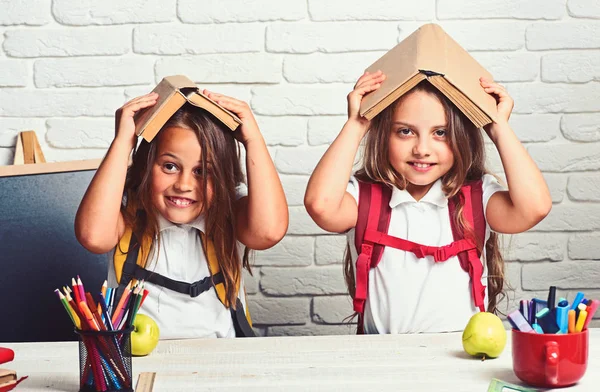 Весёлые улыбающиеся маленькие девочки с книжками на голове. Смотрю в камеру. Школьная концепция. Вернуться в школу . — стоковое фото