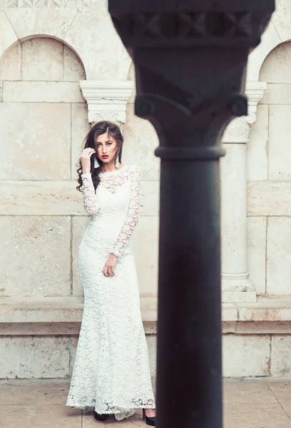 Modèle beauté avec look glamour et maquillage. Femme sensuelle pose à la colonne. Femme aux longs cheveux bruns. Mariée avec visage maquillé. Mode fille en robe de mariée blanche . — Photo