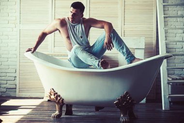 Banyo, hijyen adam. Seksi maço kolsuz bluz ve kot moda. Banyo adam otur. Fitness modeli güçlü beden sağlığı ile. Hijyen ve banyo kavramı