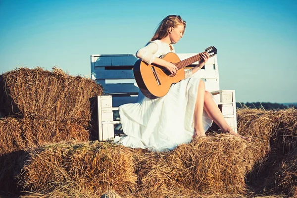 Mujer sensual tocar la guitarra en el banco de madera. Mujer guitarrista realizar concierto de música. Chica albina sostener la guitarra acústica, instrumento de cuerda. Músico de moda en vestido blanco en la naturaleza soleada — Foto de Stock
