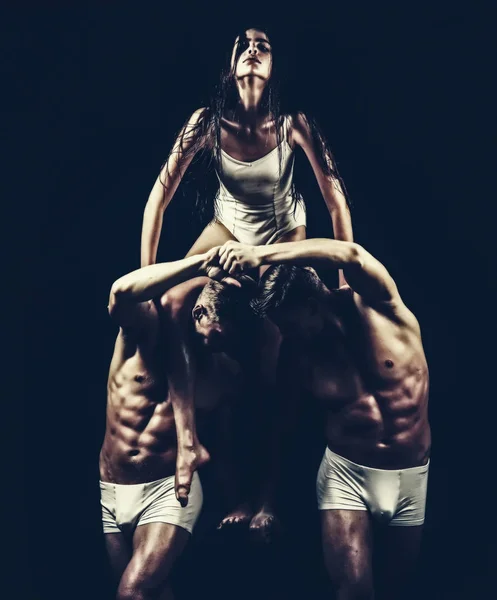 Gêmeos homens com corpo muscular e treinador menina. gêmeos com corpo forte segurar menina ginasta isolado em preto . — Fotografia de Stock